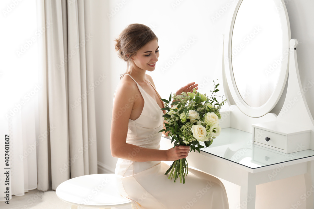 Young bride in wedding dress with beautiful bouquet near mirror indoors Young bride in wedding dress with beautiful bouquet near mirror indoors