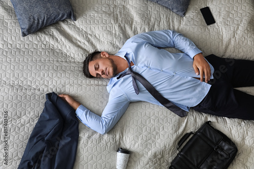 Fotografie Exhausted businessman in office wear sleeping on bed at home after work, top vie