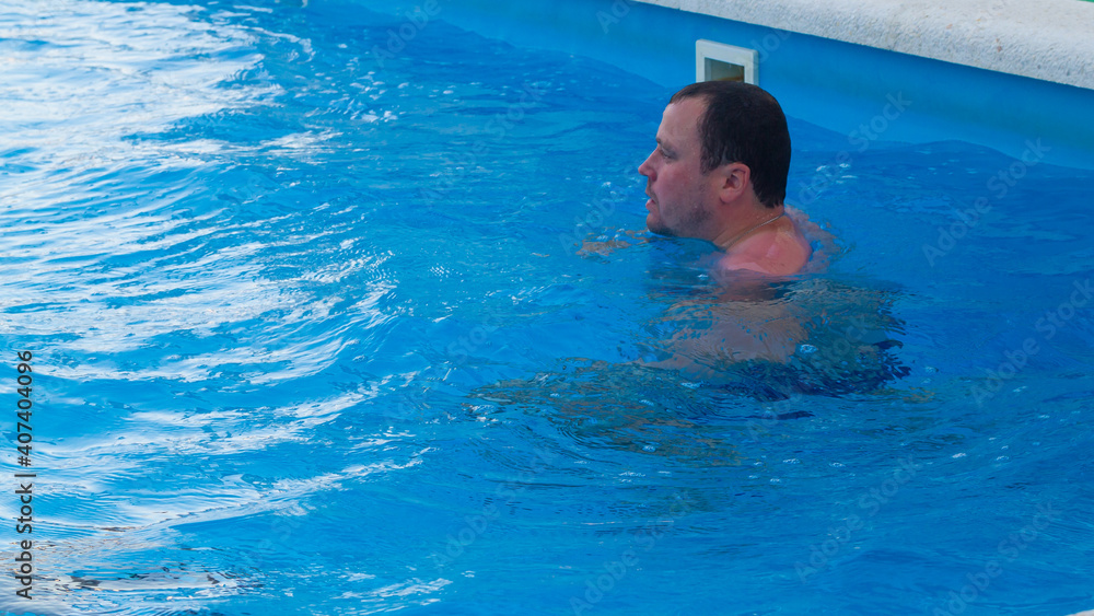 A man swims in the pool in hot summer weather on vacation.