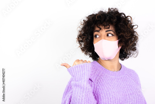 Charming young beautiful caucasian woman wearing medical mask standing against white wall looking at copy space having advertisements