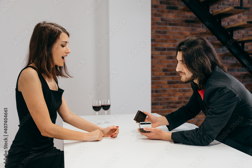 The woman is delighted. The man makes a marriage proposal to his beloved woman by opening a box with a ring. The woman is delighted. The man makes a marriage proposal to his beloved woman by opening a box with a ring.