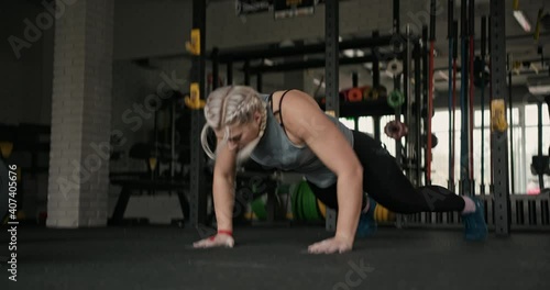 Tracking shot of blond female athlete doing squat thrust exercise during intense workout in gym