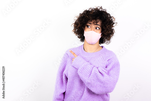 young beautiful caucasian woman wearing medical mask standing against white wall Pointing aside worried and nervous with forefinger, concern and surprise concept. © Roquillo