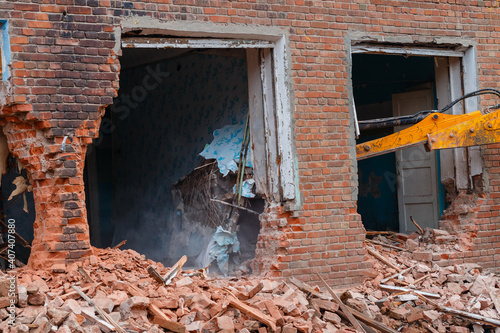 excavator disassembles the house, hydraulic bucket in the window of the building, work on dismantling old houses