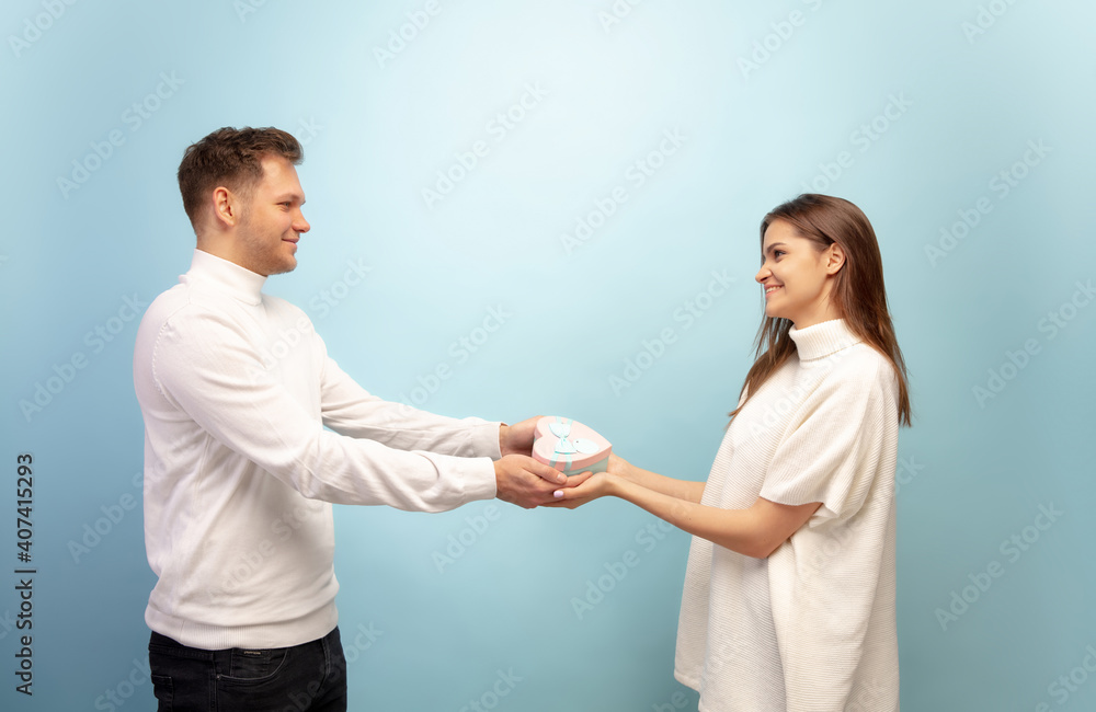 White heart. Beautiful couple in love on blue studio background. Saint Valentine's Day, love, relationship and human emotions concept. Copyspace. Young man and woman look happy together. White heart. Beautiful couple in love on blue studio background. Saint Valentine's Day, love, relationship and human emotions concept. Copyspace. Young man and woman look happy together.