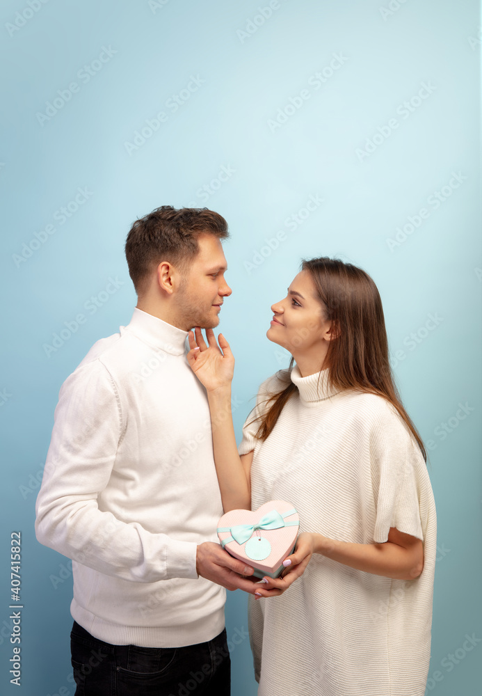White heart. Beautiful couple in love on blue studio background. Saint Valentine's Day, love, relationship and human emotions concept. Copyspace. Young man and woman look happy together. White heart. Beautiful couple in love on blue studio background. Saint Valentine's Day, love, relationship and human emotions concept. Copyspace. Young man and woman look happy together.