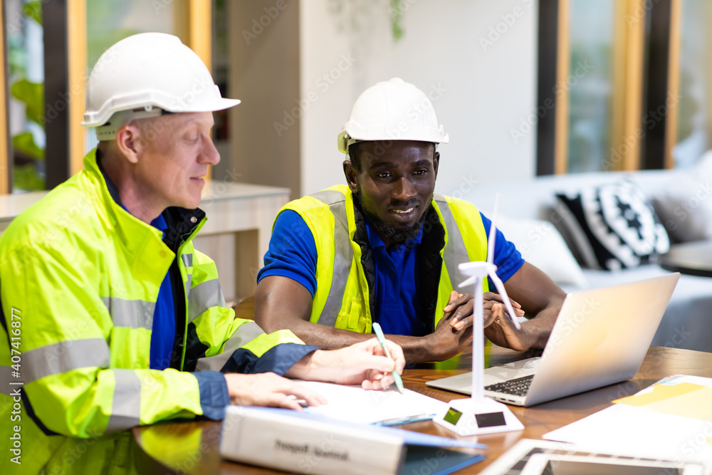 Two engineers African american engineer and caucasian electrician wearing white hard hat working on laptop computer at workplace office. clean and green alternative energy concept. Two engineers African american engineer and caucasian electrician wearing white hard hat working on laptop computer at workplace office. clean and green alternative energy concept.