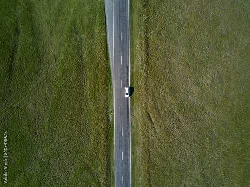 Aerial top view from car riding on straight road with green grass on both sides