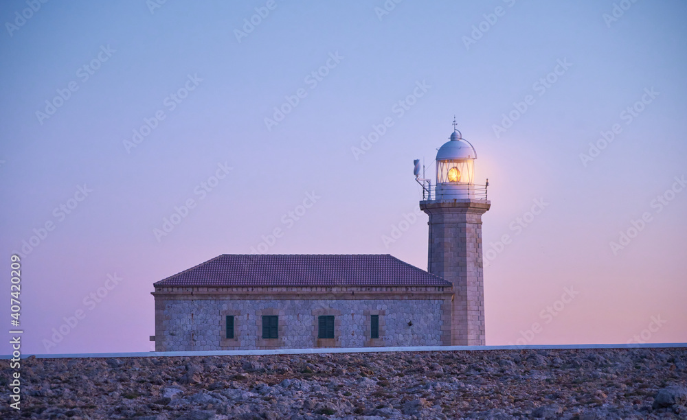 Punta Nati lighthouse in Menorca turns on at blue hour, soft background