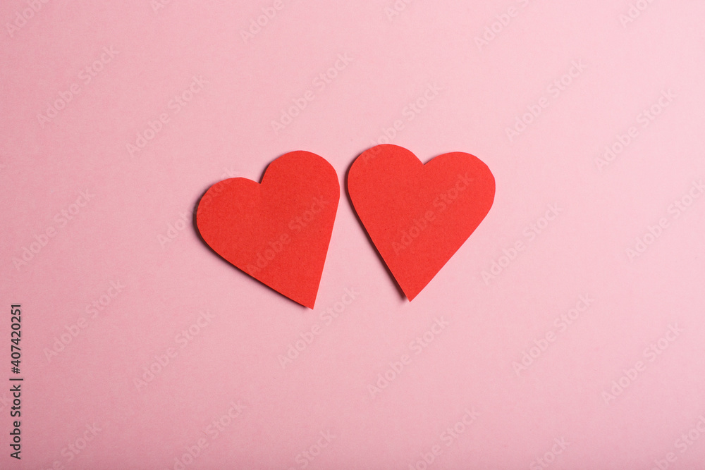 Two paper hearts on pink background.