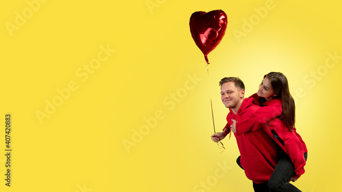 Piggyback, flyer. Beautiful couple in love on yellow studio background. Saint Valentine's Day, love, relationship and human emotions concept. Copyspace. Young man and woman look happy together.