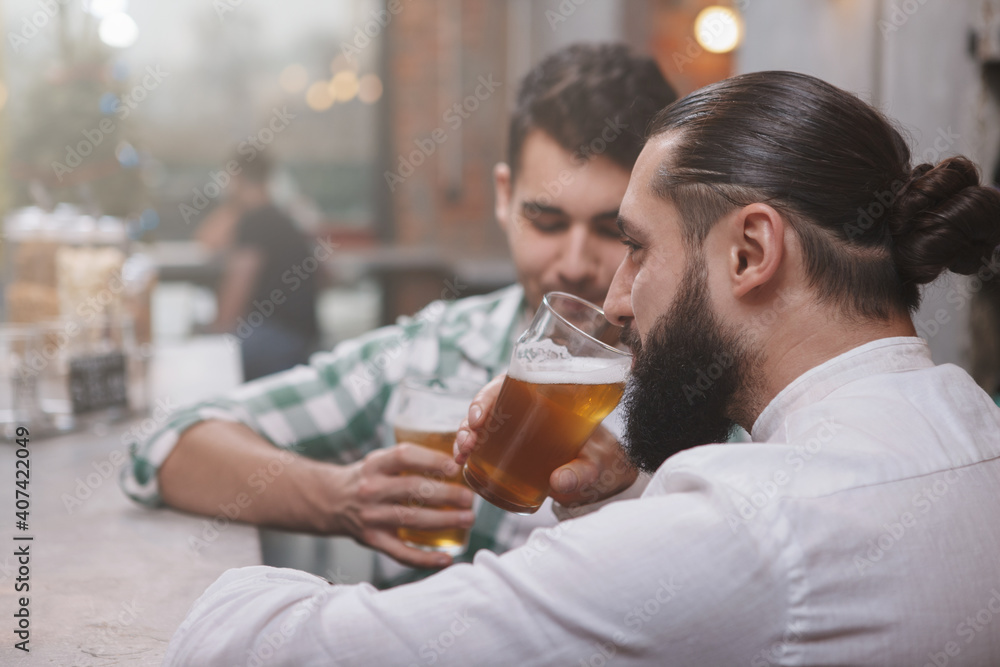 Rear view shot of a bearded man drinking beer at the pub with his friend