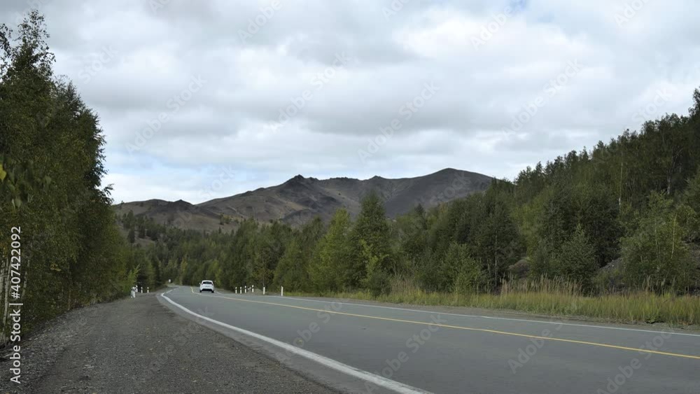 A white car drives past the camera on the highway towards a mountain of mining waste A white car drives past the camera on the highway towards a mountain of mining waste