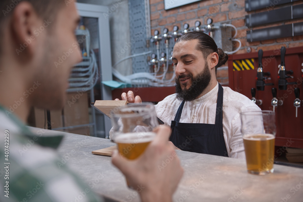 Bearded bartender typing on digital tab preparing checkout bill for the customer Bearded bartender typing on digital tab preparing checkout bill for the customer