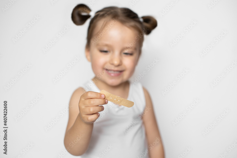 Wound, cut, medicine and healthcare concept. Close up studio shot of happy smiling little kid girl, holding in hands adhesive plaster bandage and looking at it. Focus on the plaster Wound, cut, medicine and healthcare concept. Close up studio shot of happy smiling little kid girl, holding in hands adhesive plaster bandage and looking at it. Focus on the plaster