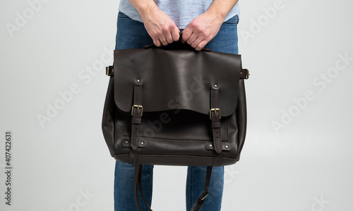 Brown men's shoulder leather bag for a documents and laptop holds by man in a blue shirt and jeans with a white background. Satchel, mens leather handmade briefcase.
