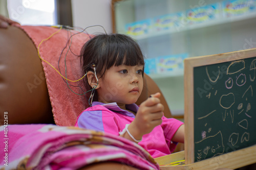 A little girl is wearing a hearing aid and is doing a neurofeedback exam. Making EEG electrodes.