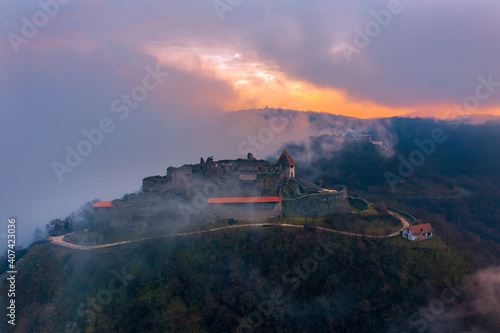 Visegrad, Hungary - Aerial panoramic drone view of the beautiful high castle of Visegrad on a moody winter morning. Danube Bend (Dunakanyar) under fog and amazing golden sunrise at background.
