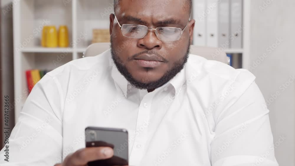 Workplace of freelancer. African-American man works at home office using smartphone. Employee is having a conference call. Remote job concept. Workplace of freelancer. African-American man works at home office using smartphone. Employee is having a conference call. Remote job concept.