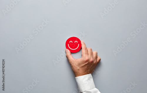 Businessman hand holding a red badge with a smiling face icon. Customer satisfaction or positive feedback