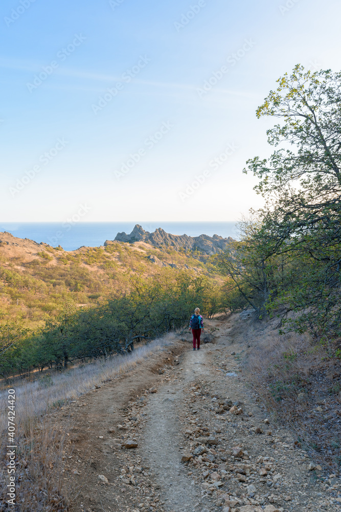 a female tourist walks along a mountain trail, at sunset, a panorama of a mountain range on the horizon .vertical photo