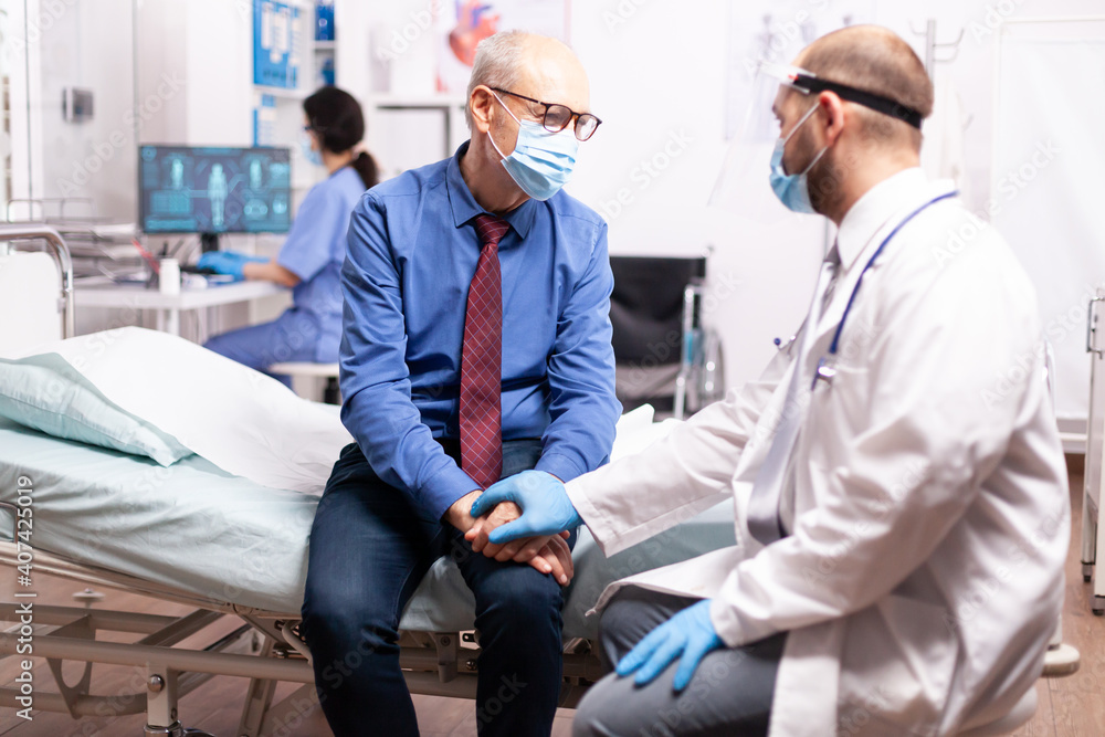 Giatric worker offering compassion to senior man in private clinic. Medical staff wearing surgical face mask talking with elderly patient during coronavirus pandemic. Giatric worker offering compassion to senior man in private clinic. Medical staff wearing surgical face mask talking with elderly patient during coronavirus pandemic.