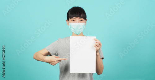 Empty space for text..Asian woman is holding and poniting blank A4 paper and wear face mask or medical mask on blue and green or mint background. photo