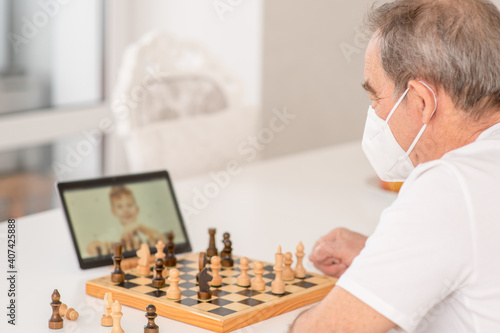 Senior grandfather uses tablet computer to play chess with his grandson during quarantine Coronavirus (Covid-19) epidemic