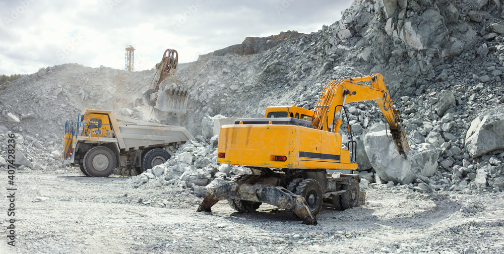 Hydraulic breaker, close-up, working in a stone quarry, with heavy mining dump truck during of loading in the background, panorama. Hydraulic breaker, close-up, working in a stone quarry, with heavy mining dump truck during of loading in the background, panorama.