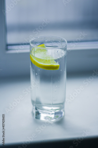 A glass of water with a slice of lemon stands on a white windowsill by the window