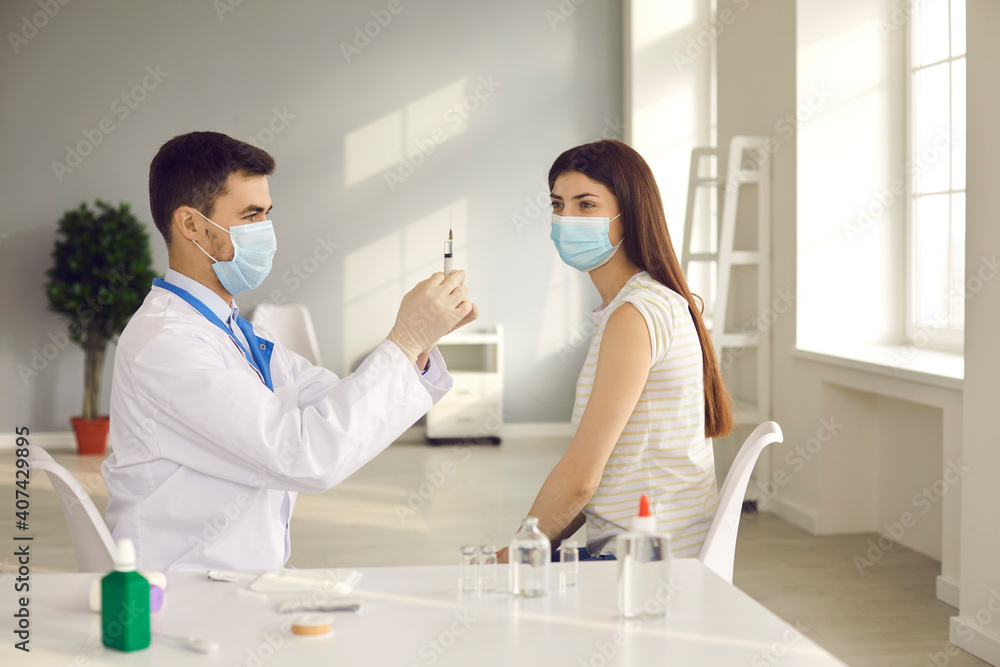 Man doctor in uniform and medical mask preparing syringe before making vaccination agaist COVID-19 infection during pandemic for woman in medical clinic. Vaccine, vaccination, virus protection concept Man doctor in uniform and medical mask preparing syringe before making vaccination agaist COVID-19 infection during pandemic for woman in medical clinic. Vaccine, vaccination, virus protection concept