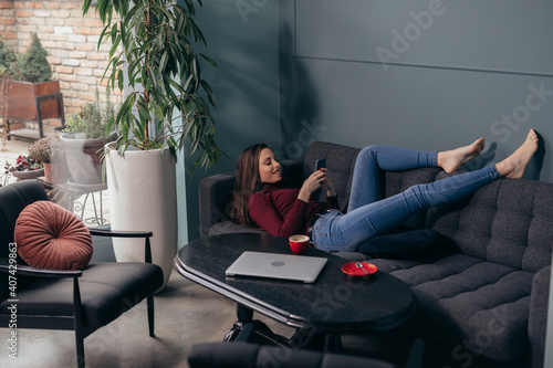 woman relaxing at her home, using lsmartphone and drinking coffee photo