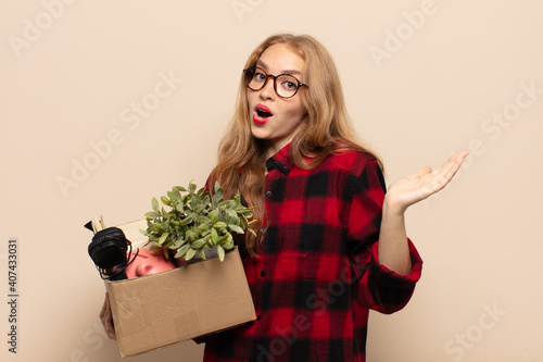 blonde woman looking surprised and shocked, with jaw dropped holding an object with an open hand on the side photo