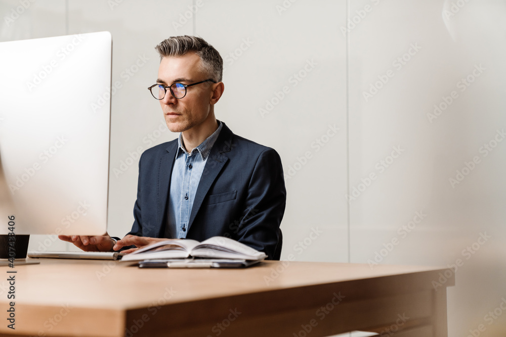 Focused grey man working with computer while sitting at table in office Focused grey man working with computer while sitting at table in office