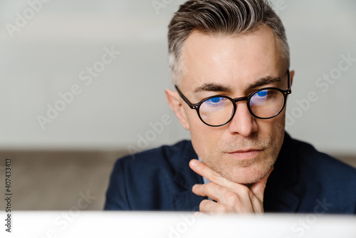 Concentrated grey man in eyeglasses working with computer at office