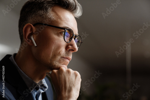 Concentrated grey man in wireless earphones working at office