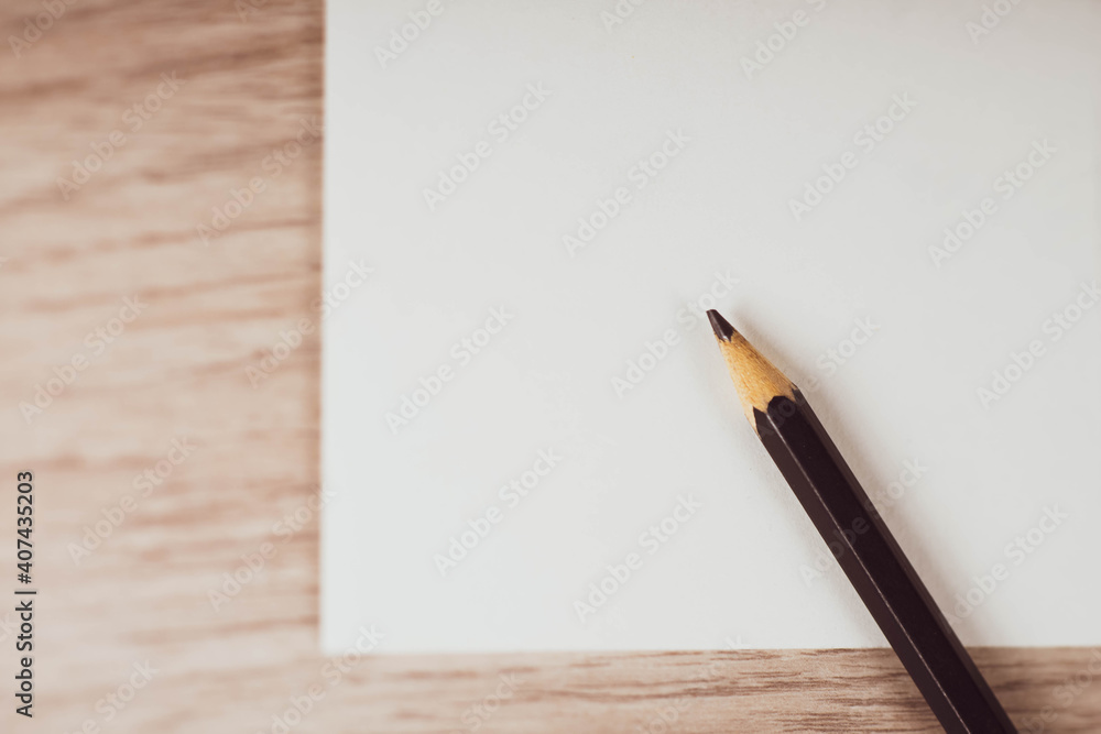 Top view of black pencil on empty white paper blanck. Wooden table background. Top view of black pencil on empty white paper blanck. Wooden table background.