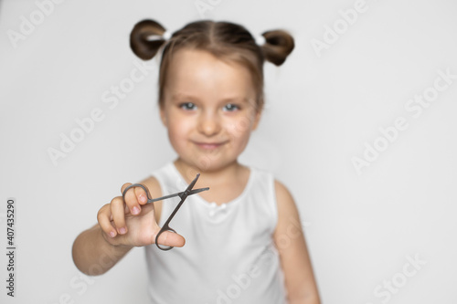 Happy 3 years old kid girl holding scissors for trim child's fingernails, smiling to camera. Baby nails hygiene concept. Close up, isolated on white. Focus on the scissors