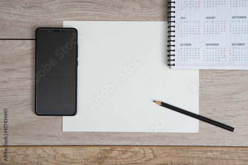 Top view of workplace. Empty paper blank, spiral calendar, black pencil and phone on wooden table. photo