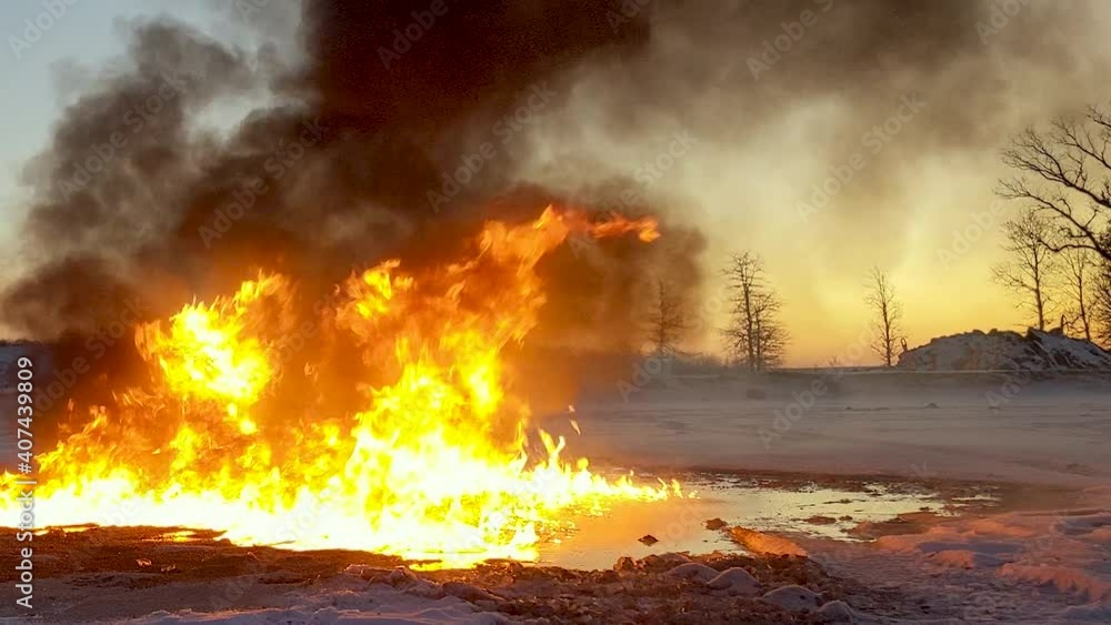 Slow zoom in on an oil burning fire. Thick black smoke rises into the sky. Melted snow surrounds the oil and fire. Slow zoom in on an oil burning fire. Thick black smoke rises into the sky. Melted snow surrounds the oil and fire.