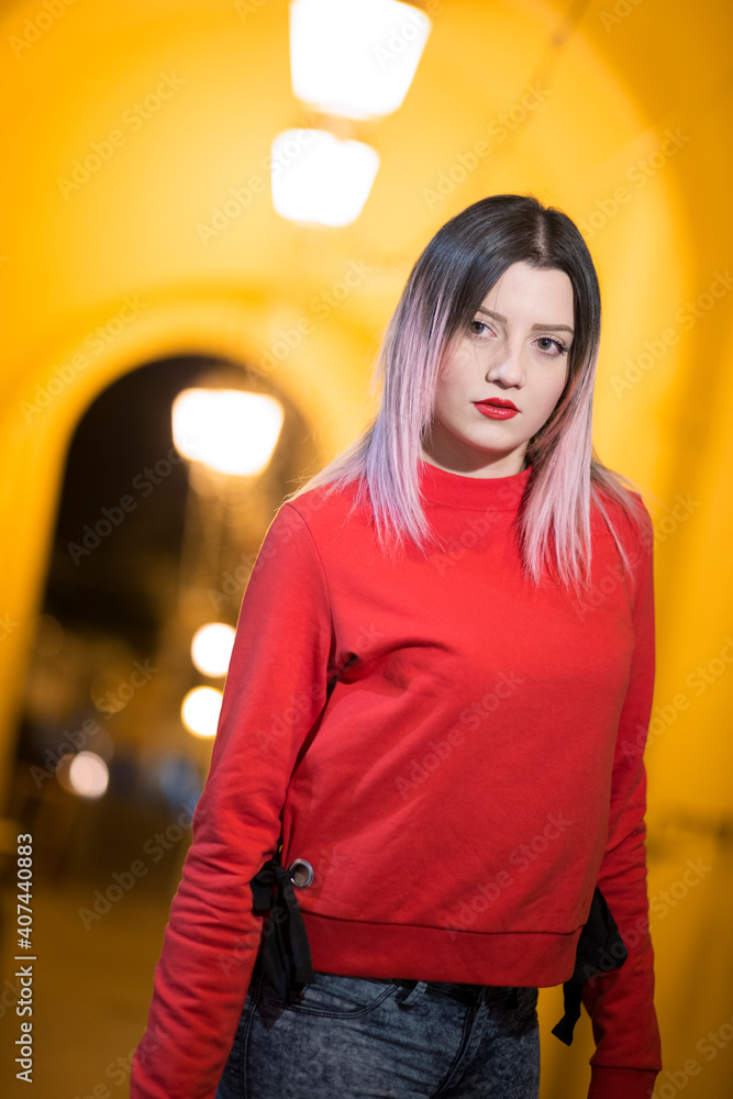 Bella ragazza con maglione rosso guarda con aria seria  in contesto urbano notturno