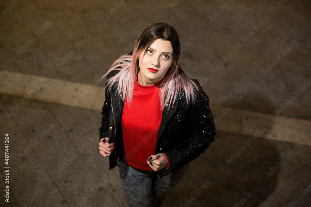 Bella ragazza bionda con cappotto nero e maglione rosso in contesto urbano guarda con aria assorta Bella ragazza bionda con cappotto nero e maglione rosso in contesto urbano guarda con aria assorta