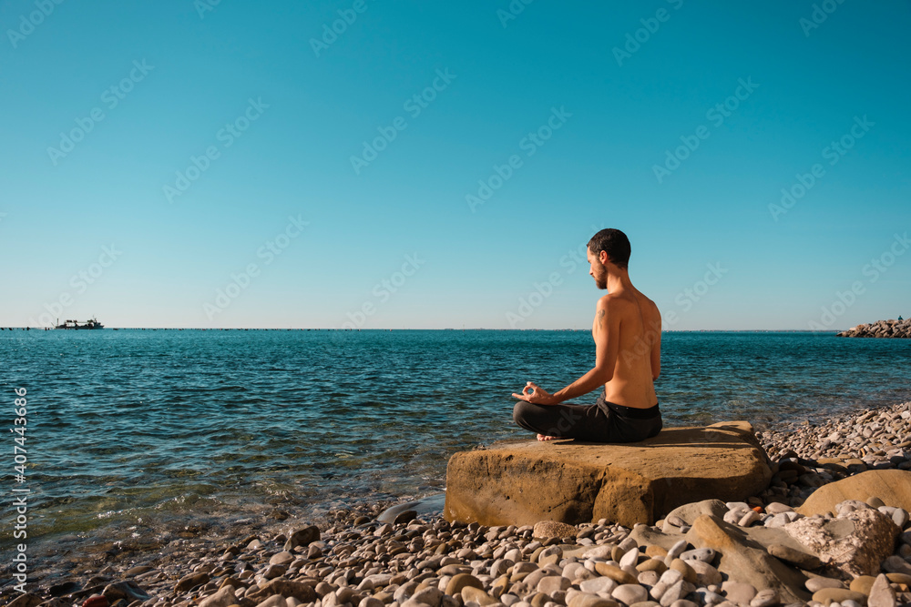 Attractive young man practicing yoga meditation and breathwork outdoors by the sea