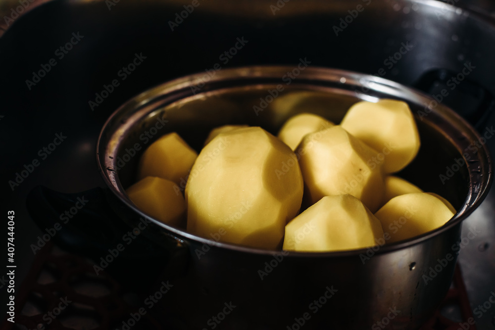 Peeled potatoes in a silver pot. Clean potatoes for cooking. Dishes with peeled potatoes, on a dark background. Peeled potatoes in a silver pot. Clean potatoes for cooking. Dishes with peeled potatoes, on a dark background.