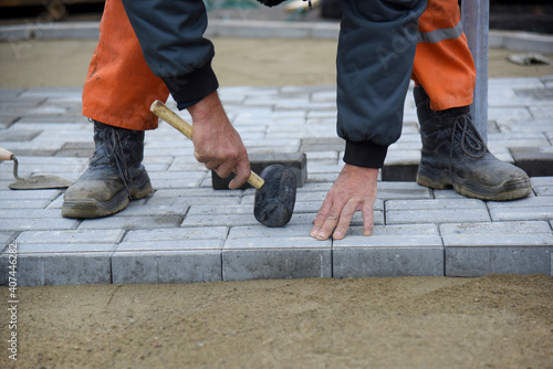 A worker knocks with a hammer, levels the paving slabs, close-up.
