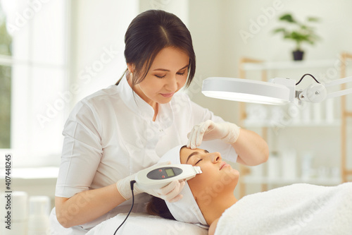 Smiling dermatologist making ultrasound apparatus facial cleaning for young woman