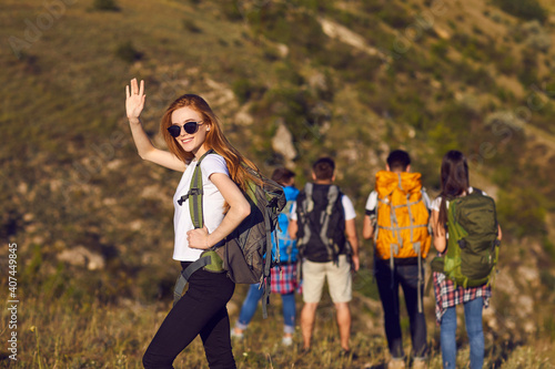 Smiling girl tourist hiker with backpack standing and waving with hand during hiking