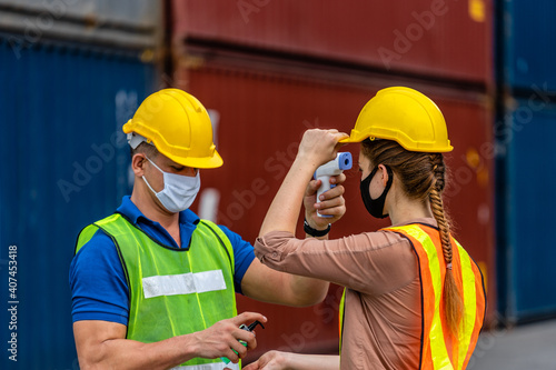 The foreman in a reflective safety vest and Yellow Helmet is checking the temperature with a thermometer. And spraying with alcohol to wash workers before entering work