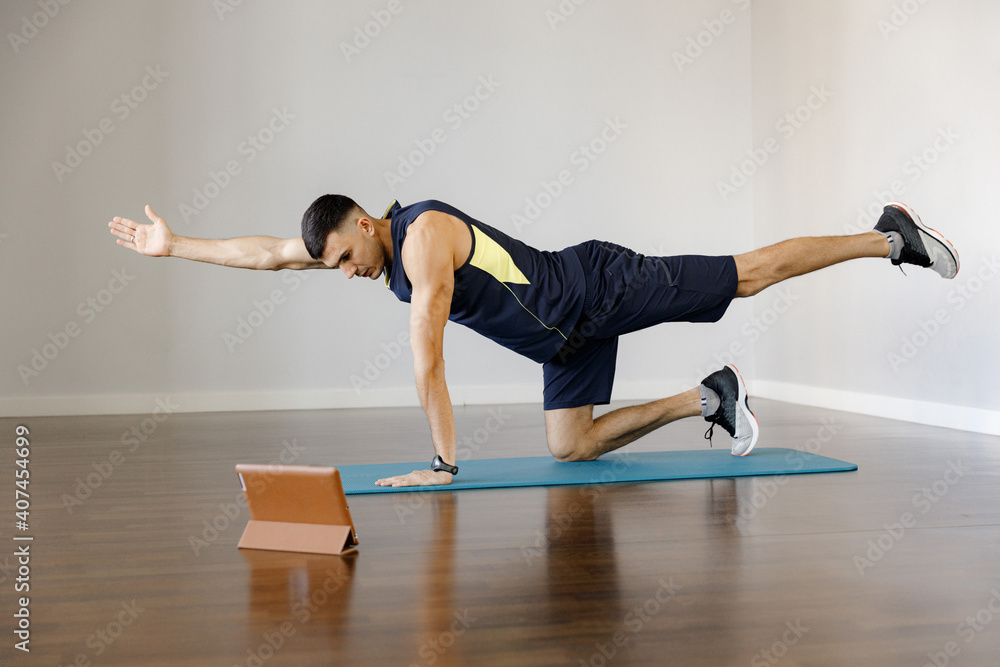 Naklejka premium A young man in sportswear does a sports exercise. Online training. Stretching your hands and feet on the app in your phone. Healthy lifestyle in self-isolation