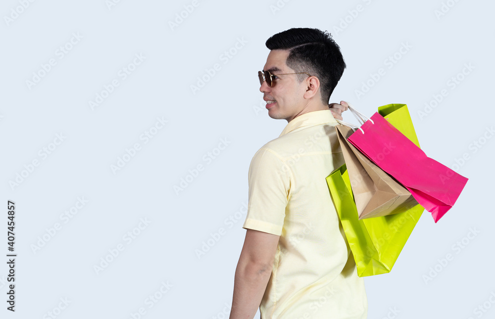 Portrait handsome young asian man wearing yellow cheerful glad content guy carrying new things colorful packages on blue background in studio. Asian man people. Portrait handsome young asian man wearing yellow cheerful glad content guy carrying new things colorful packages on blue background in studio. Asian man people.